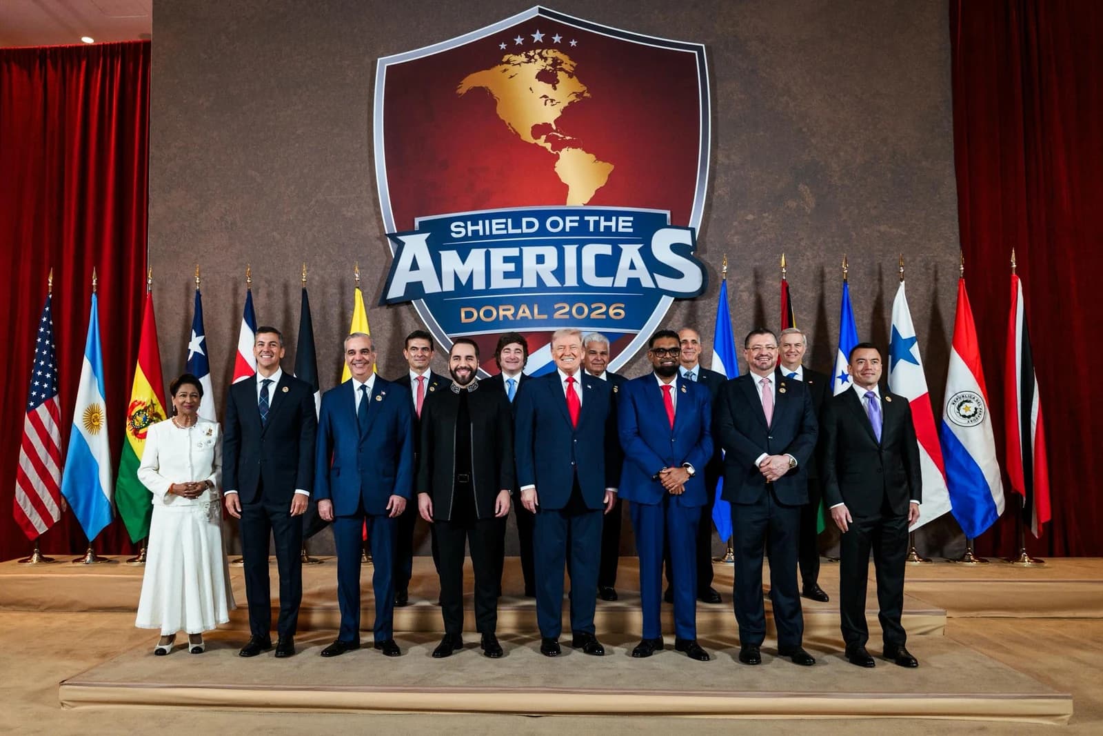 Donald Trump stands with other leaders in front of a banner and flags.