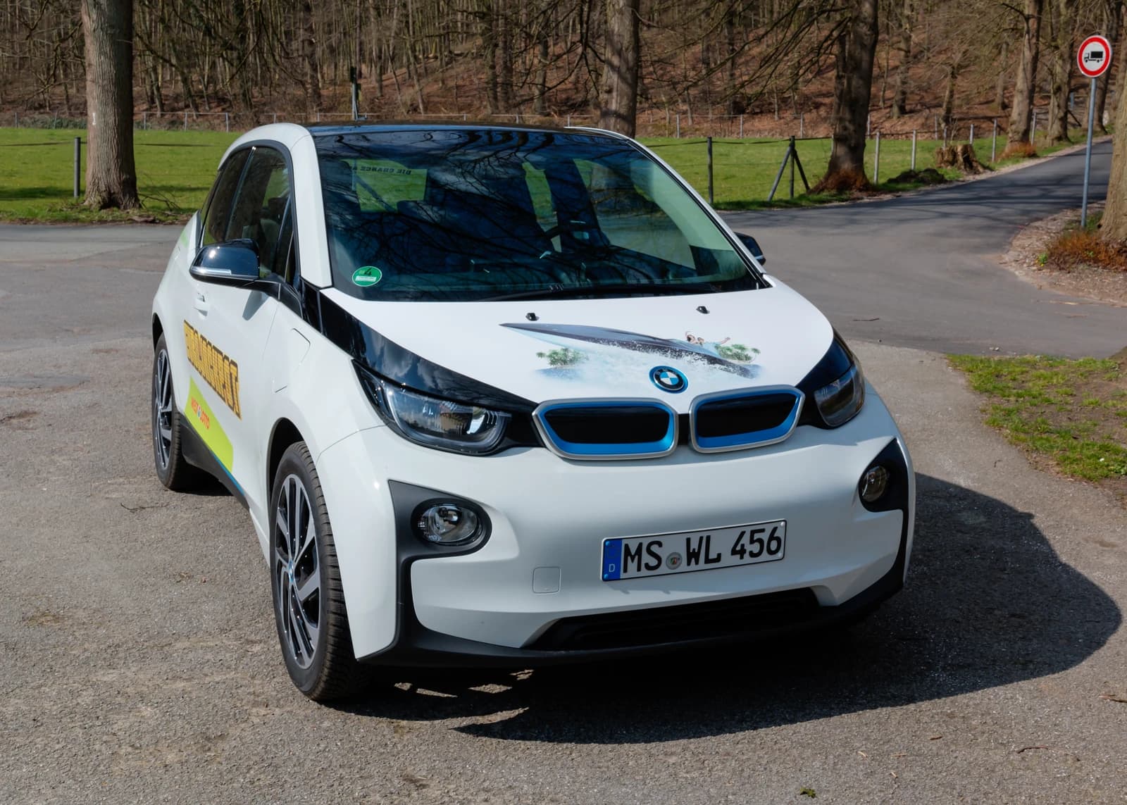 White BMW i3 electric car with blue accents parked on an unpaved road.