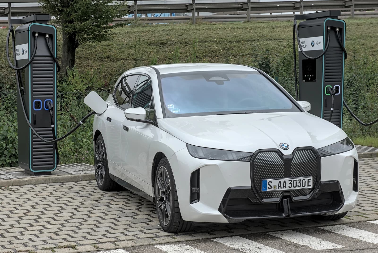 White BMW iX electric SUV connected to a charging station outdoors.