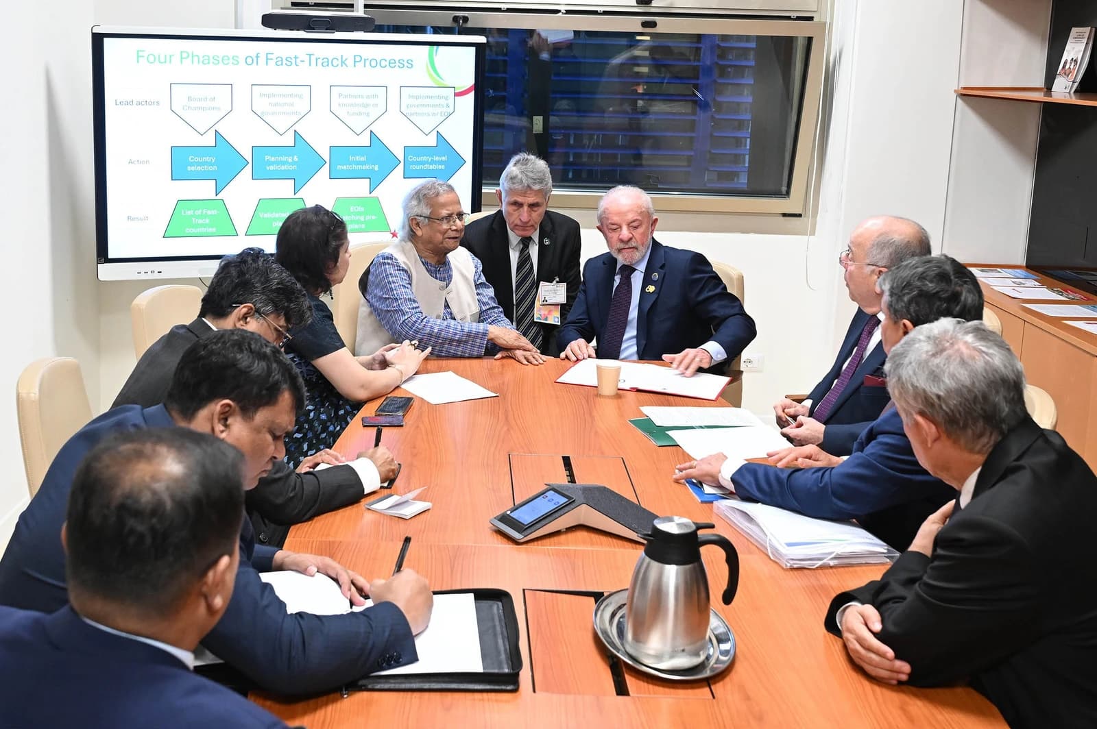 Muhammad Yunus and Luiz Inacio Lula da Silva seated at a conference table with other attendees.