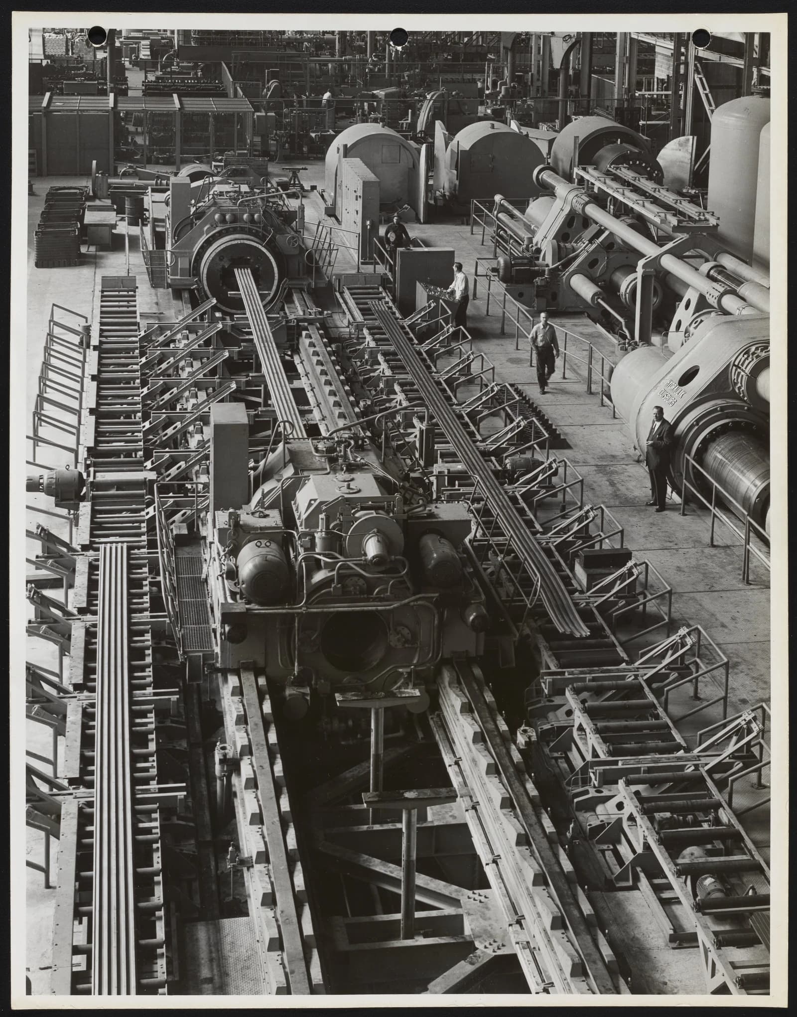 Industrial machinery in a large factory with several workers standing nearby.