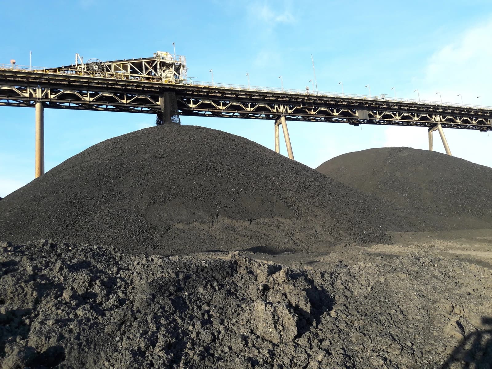 Coal piles at a mining site under a large industrial conveyor belt system.