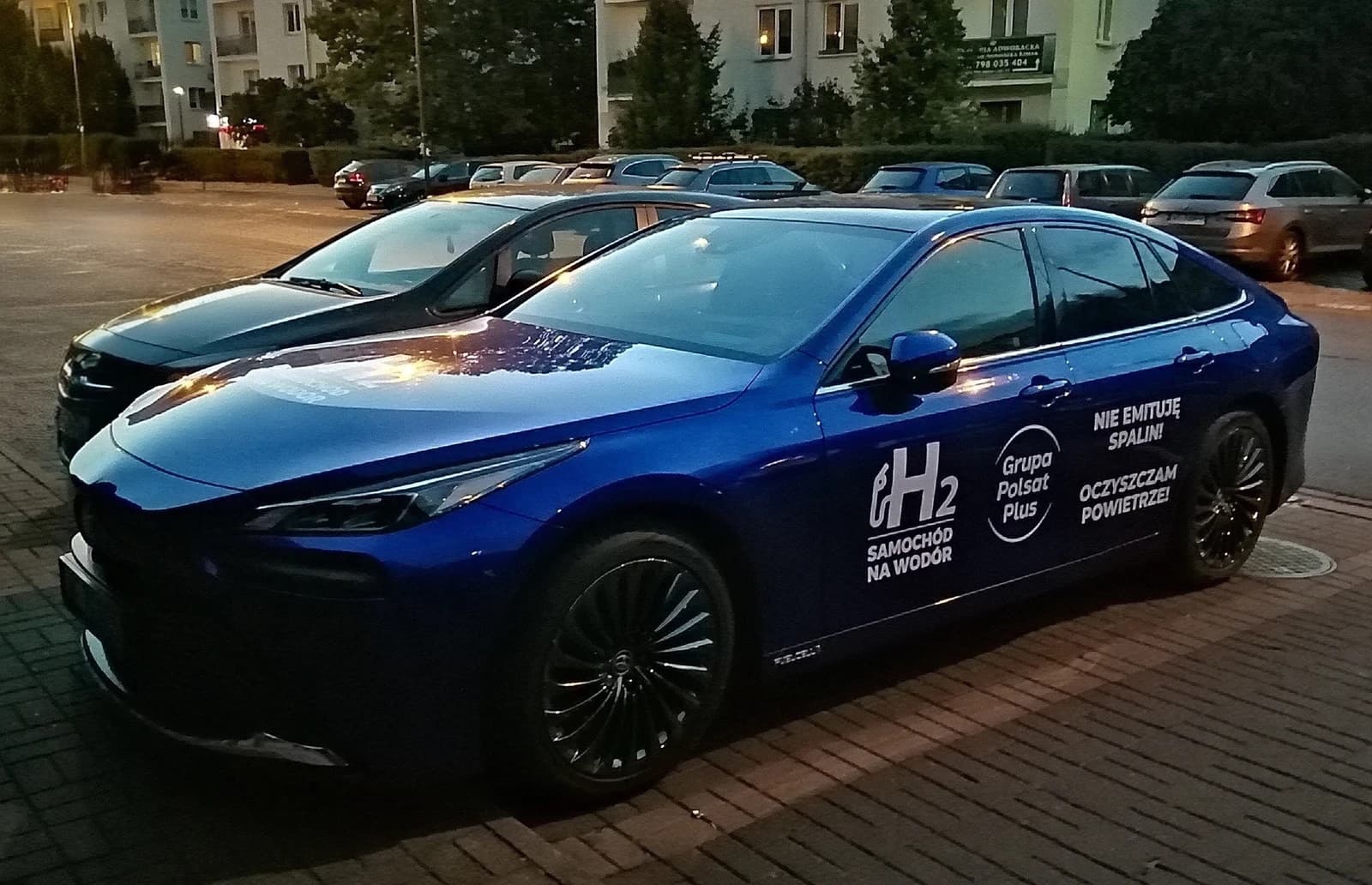 Blue Toyota Mirai II, a hydrogen fuel cell car, parked on a paved lot.