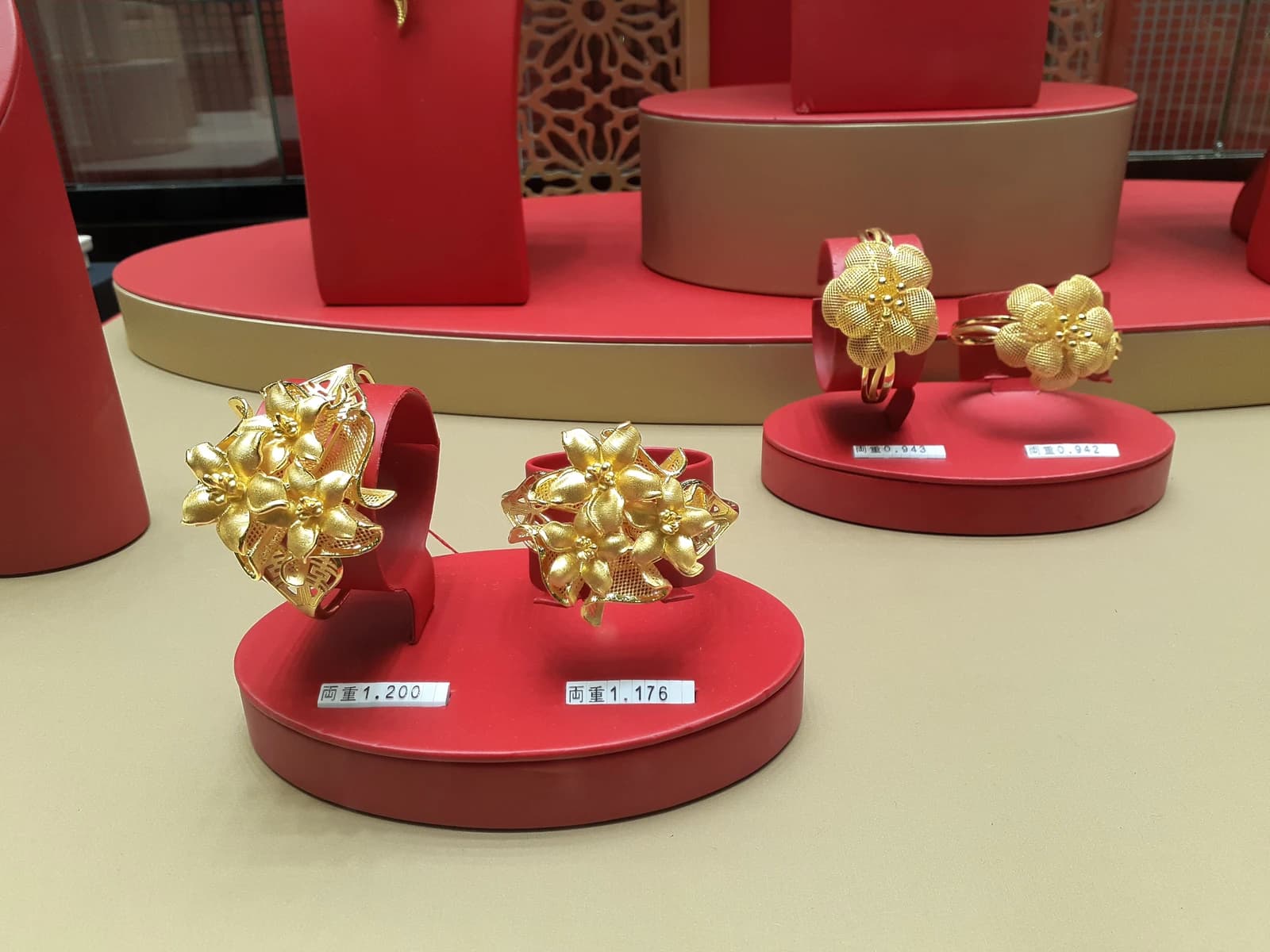 Gold jewelry, including intricate rings, displayed on red stands in a shop window.