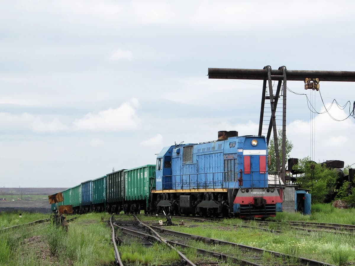 Blue TEM7A-0242 locomotive pulls green coal wagons on tracks at Kostenko mine.