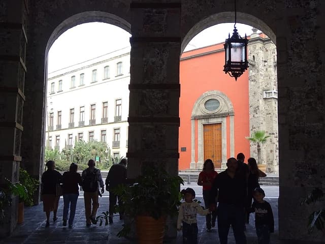 People walking through archways from a palace courtyard to a street with buildings.