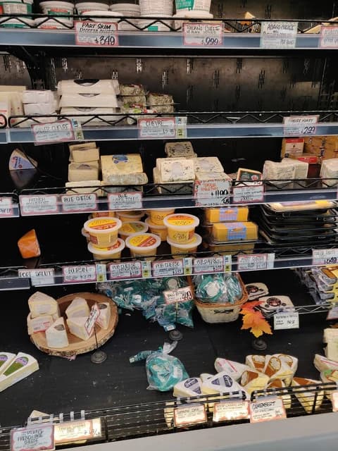 Refrigerated display case filled with a selection of cheeses and hummus at a grocery store.