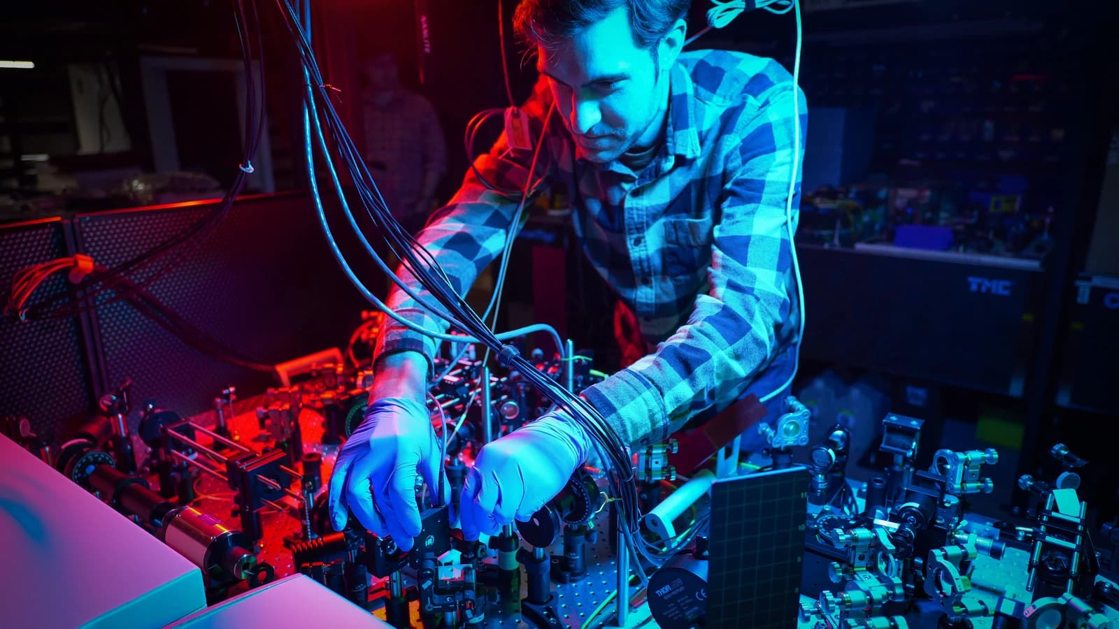 Scientist in blue gloves adjusts components on a quantum computing experimental setup.