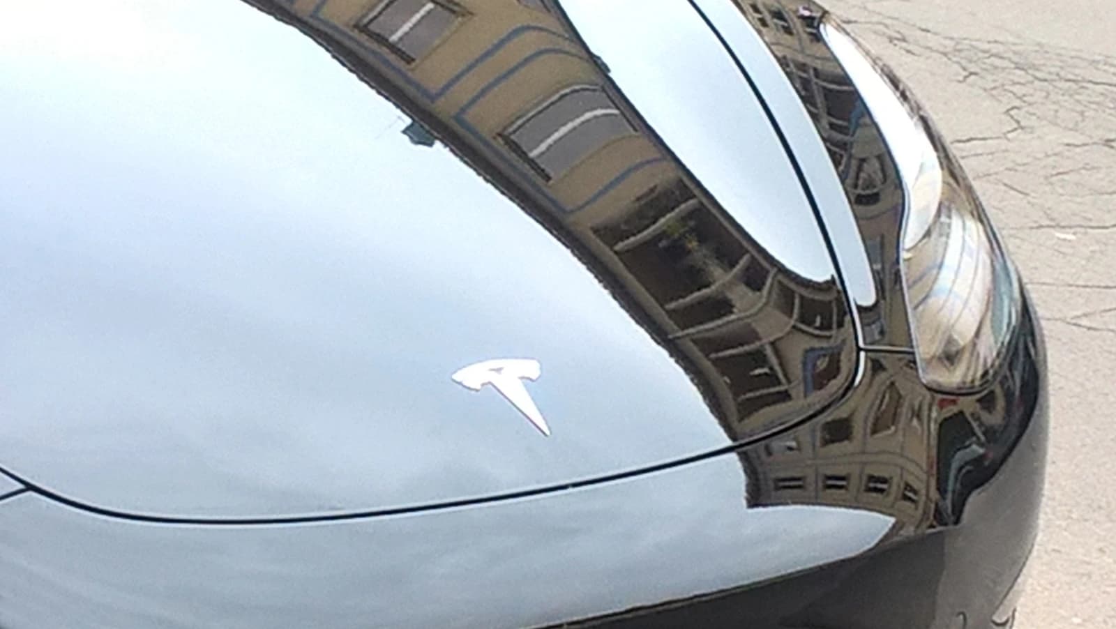 Close-up of the front hood of a black Tesla car with the Tesla logo.