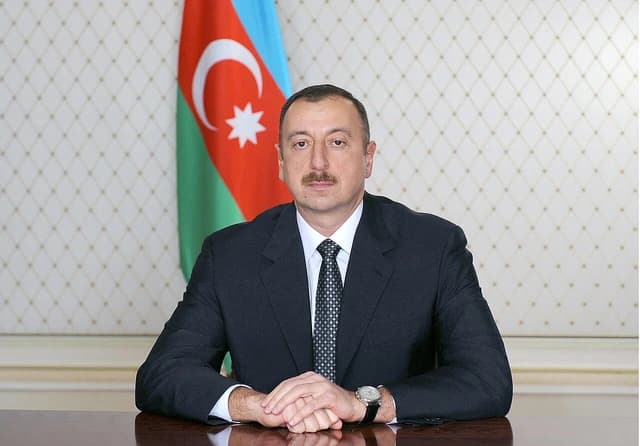 Ilham Aliyev, President of Azerbaijan, sitting at a desk with his country's flag behind him.