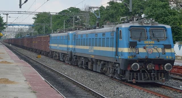 Blue Indian Railways WAG7 locomotive 28348 pulling a long train of coal wagons.