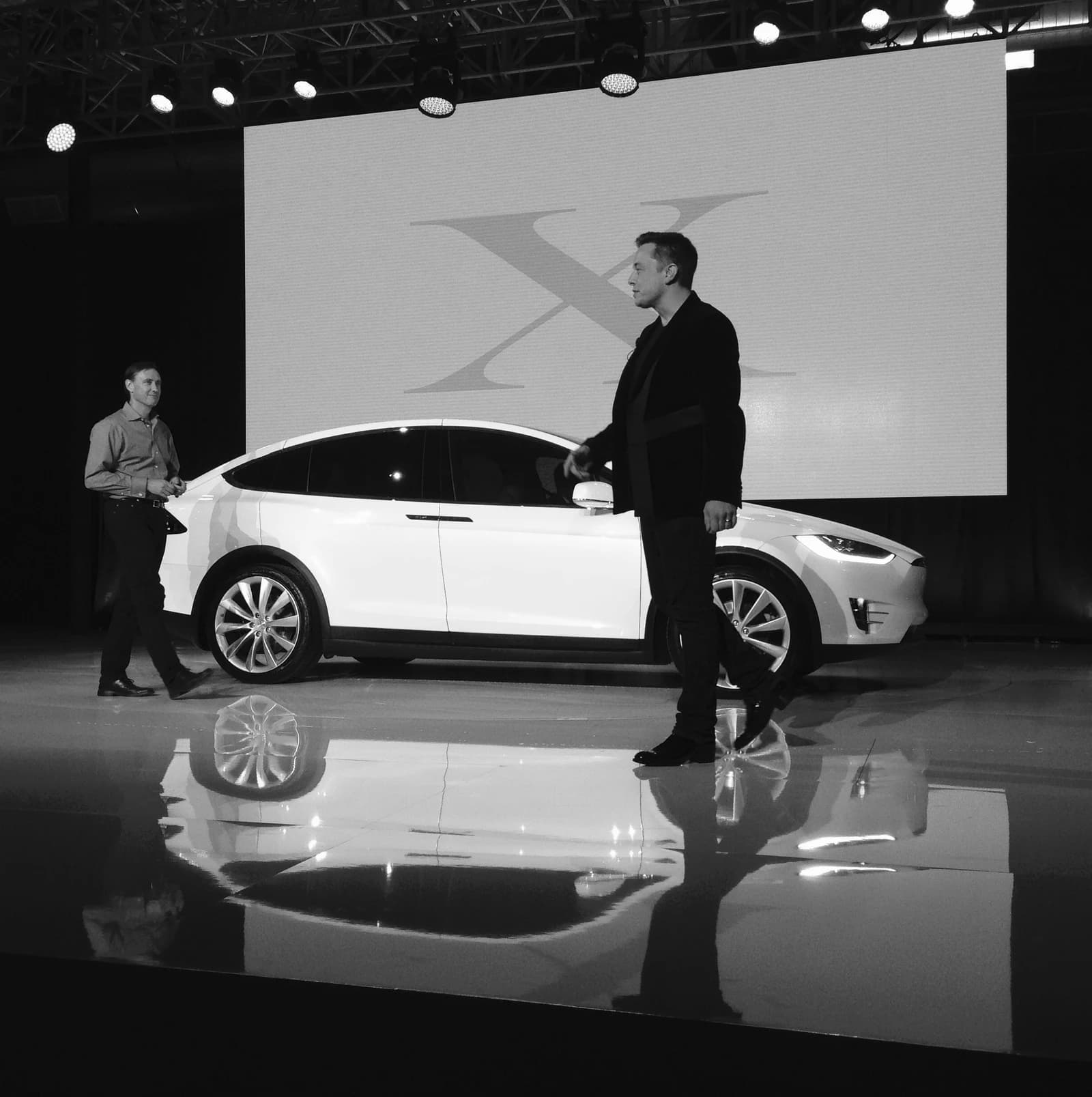 Elon Musk standing next to a white Tesla Model X on stage.