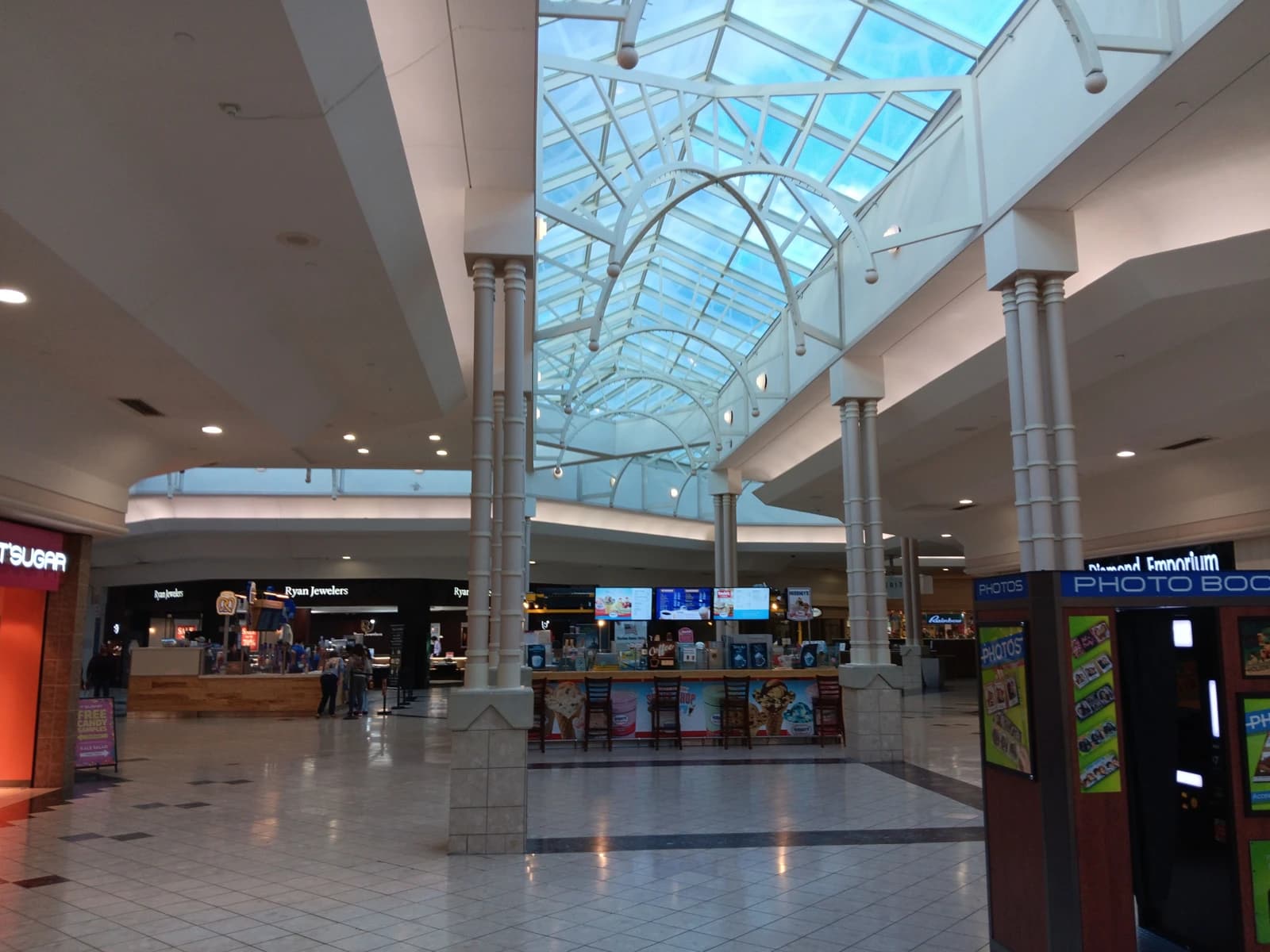An empty shopping mall interior with a glass roof and retail stores.