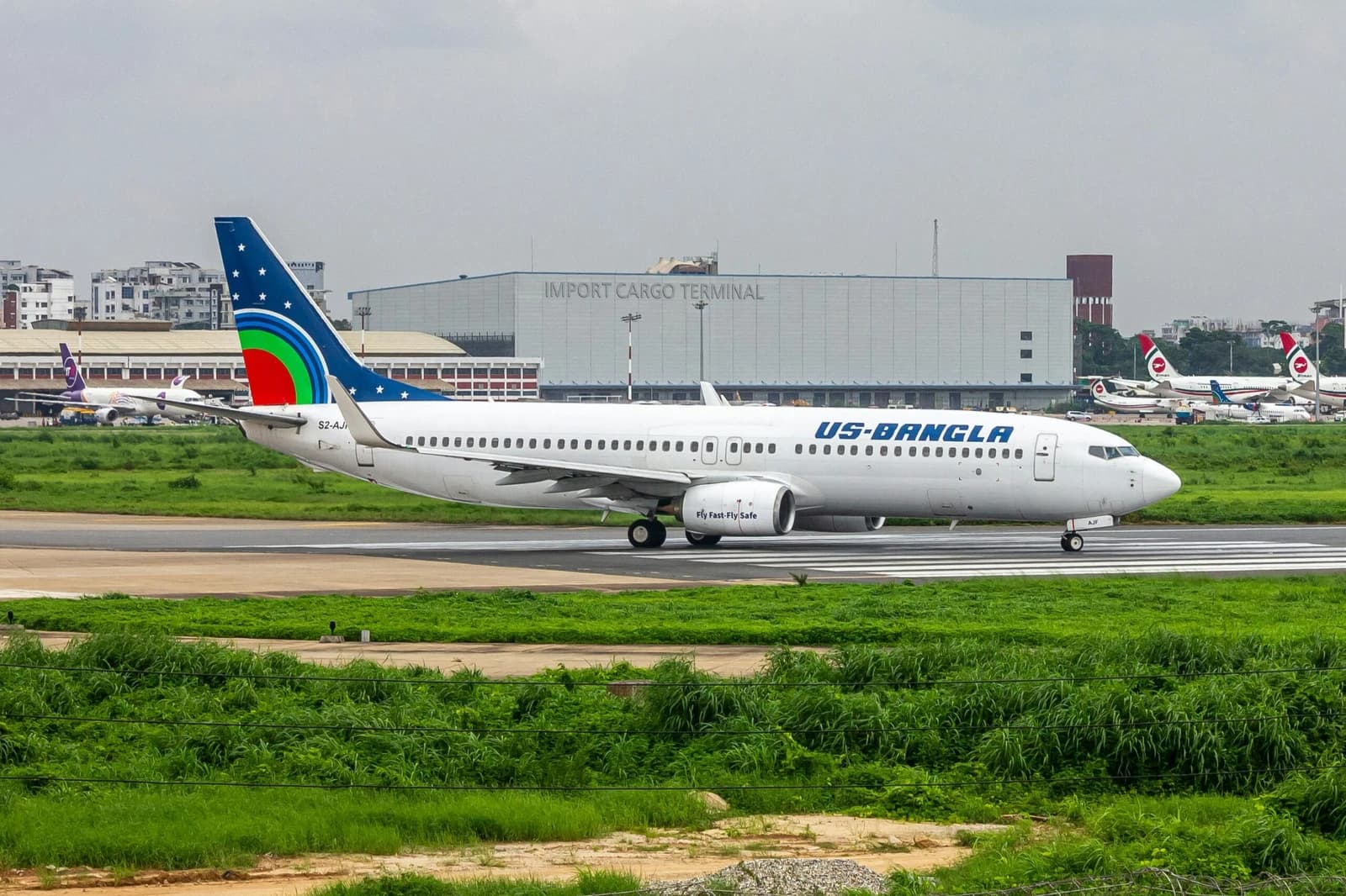 US-Bangla Airlines jetliner taxing on an airport runway with other planes and a cargo terminal.