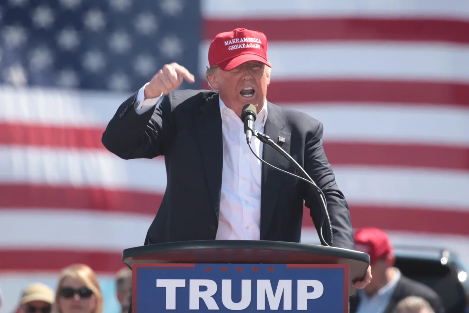 Donald Trump speaking at a podium with microphones, American flag in background.
