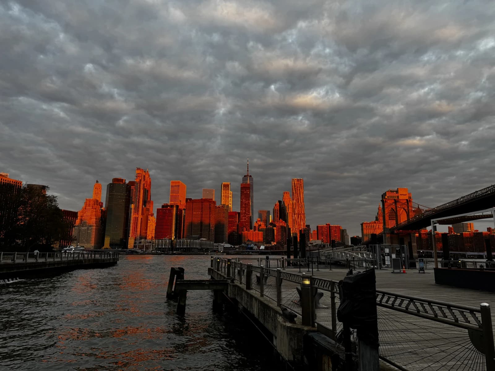 Manhattan Financial District skyline, with One World Trade Center, glows orange at sunset.