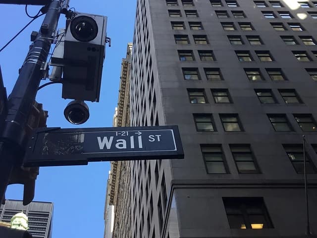 Wall Street sign on a lamppost, with tall buildings and a clear blue sky in the background.