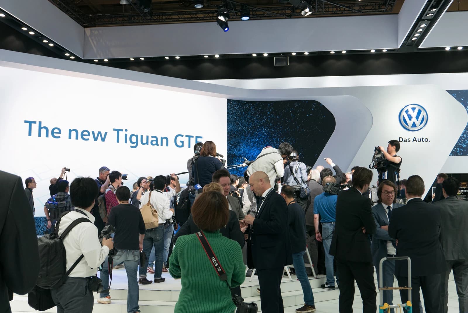 Journalists and attendees gather at the Volkswagen stand during a motor show.