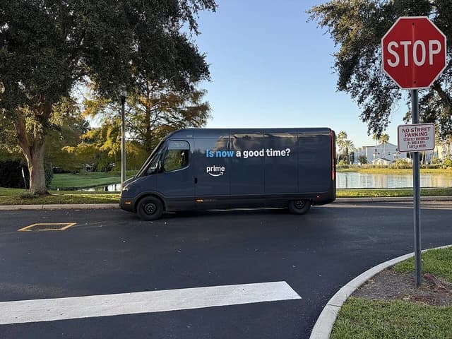 Amazon electric delivery van in a gated community with a lake and houses in the background.