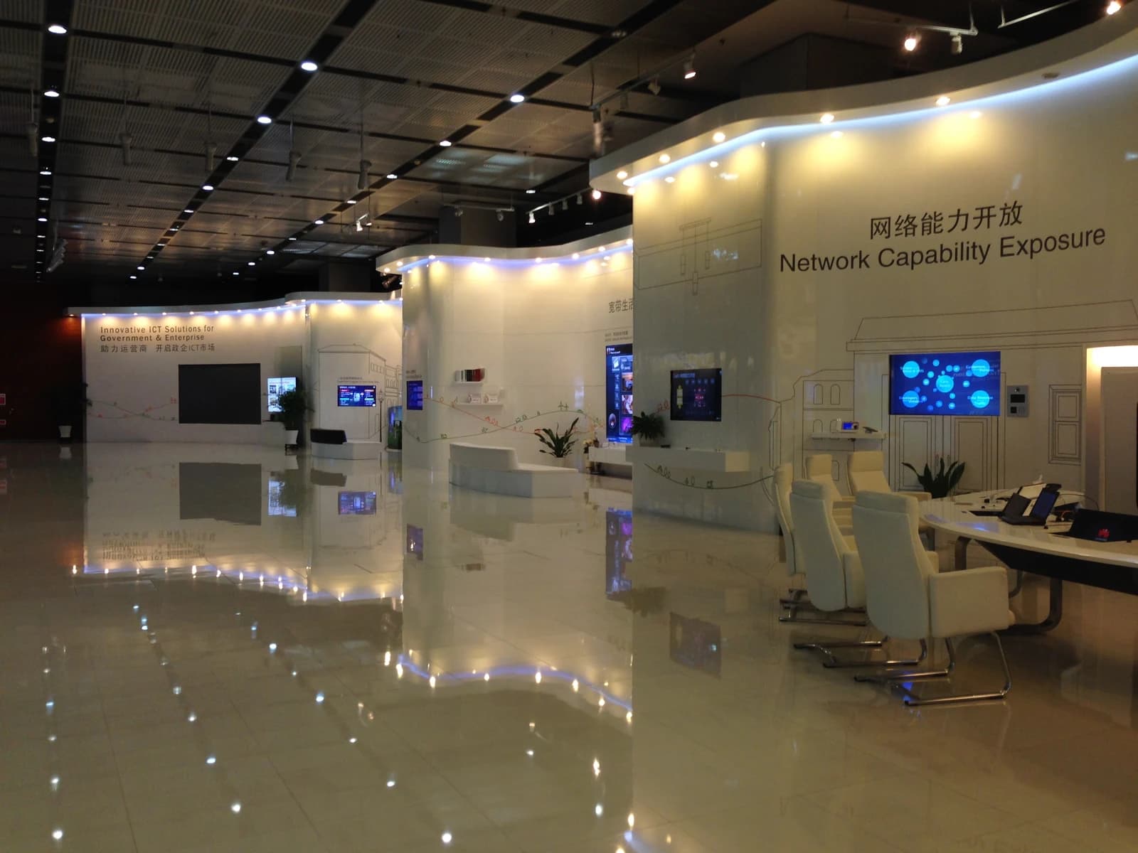 Interior view of a Huawei exhibition center with display screens and white seating.