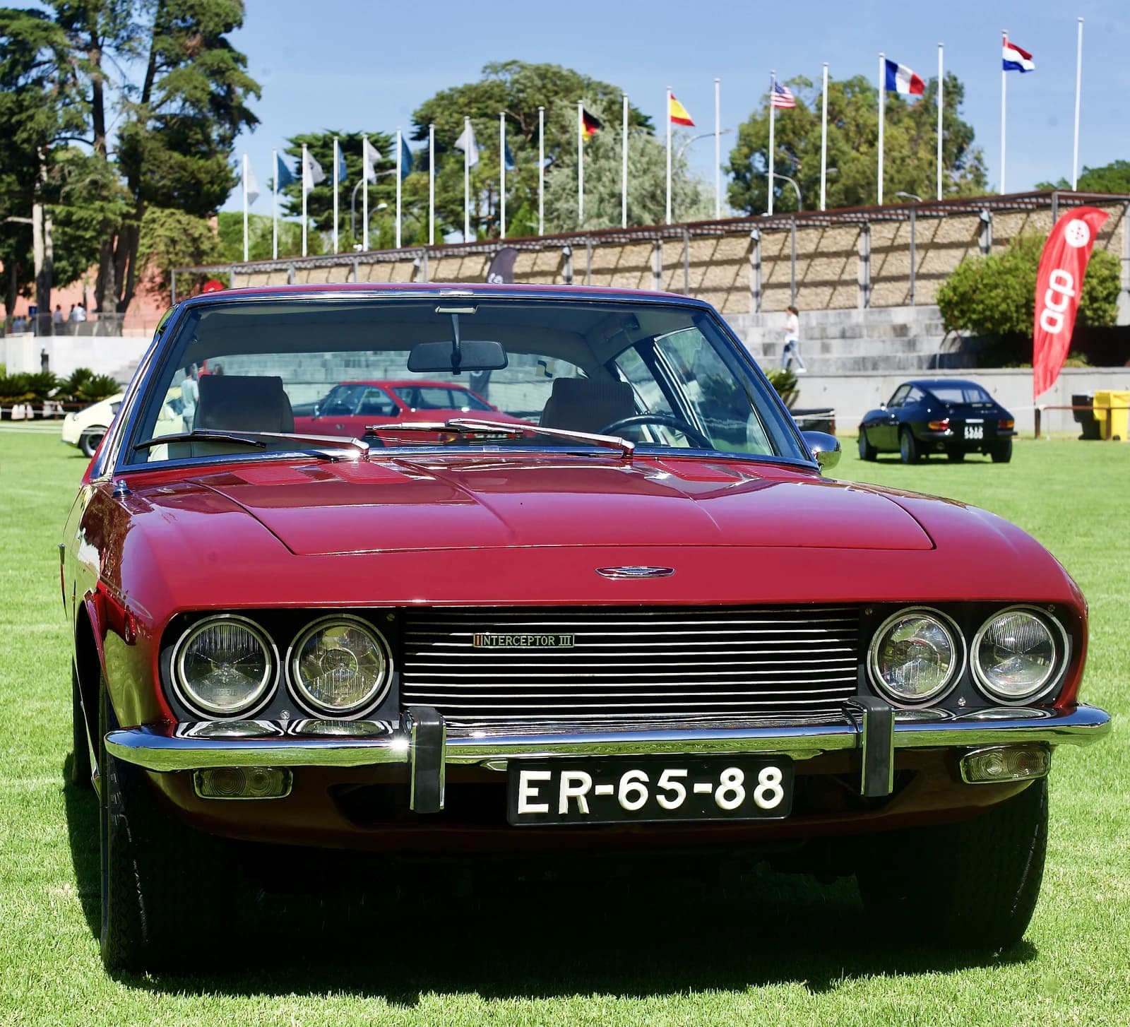 Red Jensen Interceptor III classic car parked outdoors on green grass.