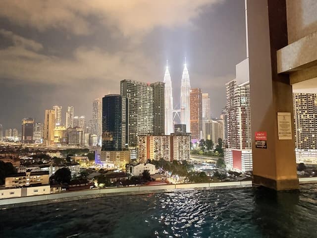 Kuala Lumpur skyline at night with illuminated Petronas Twin Towers towering over city.