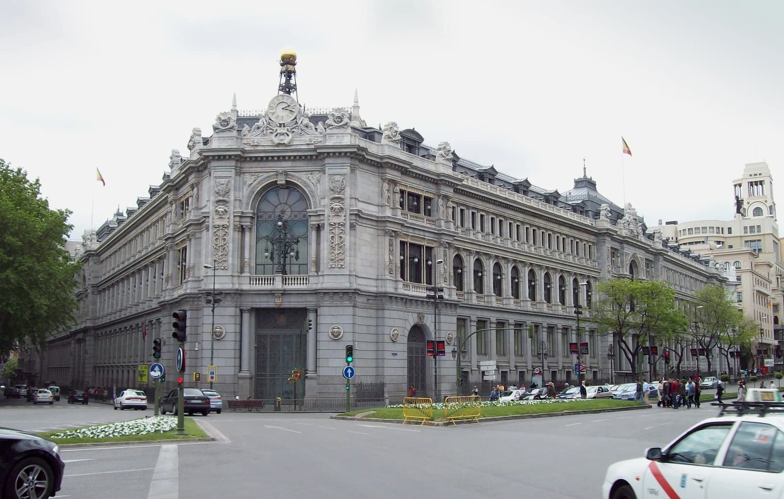 Exterior of the Banco de España, a large ornate stone building, at a street intersection.