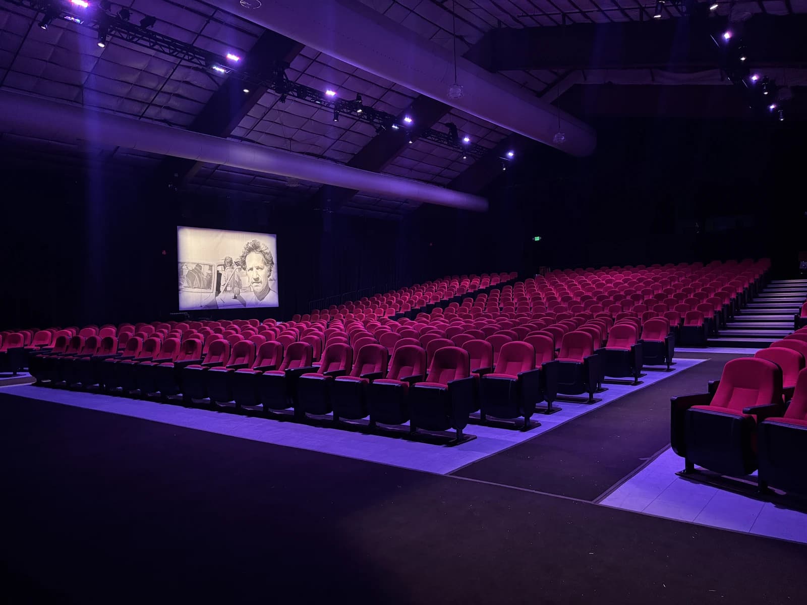 Empty auditorium with rows of red seats facing a screen displaying a film scene.