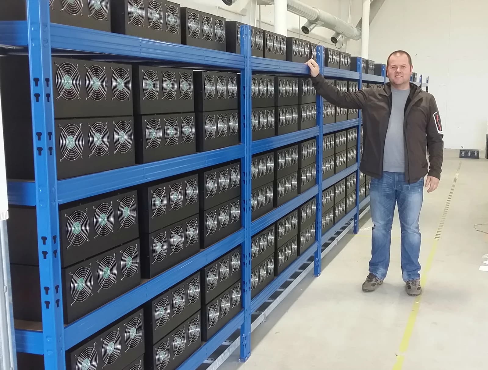 Man stands next to large racks of Bitcoin mining computers in a data center.