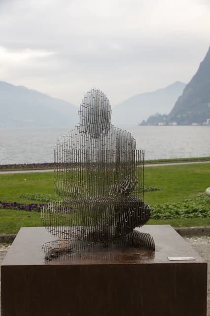 Satoshi Nakamoto metal sculpture in Lugano, Switzerland with lake and mountains.