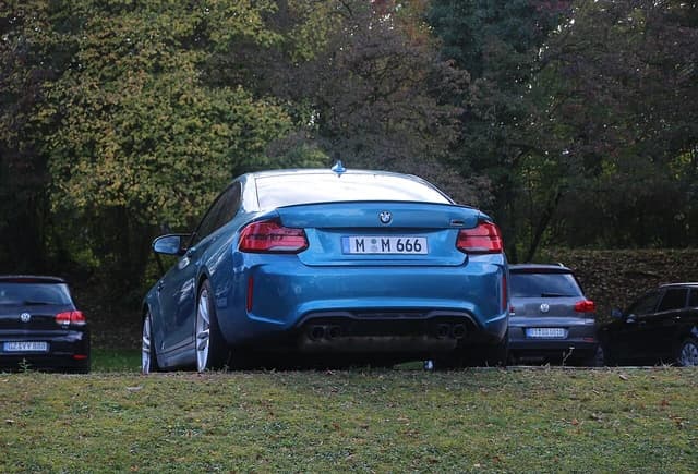 Rear view of a blue 2023 BMW M2 Competition parked on grass.
