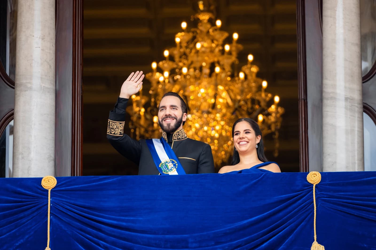 Nayib Bukele, President of El Salvador, and Gabriela de Bukele waving from a balcony.