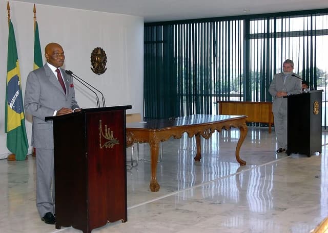 Abdoulaye Wade speaking at a podium next to two flags; Lula da Silva stands at a podium in the background.