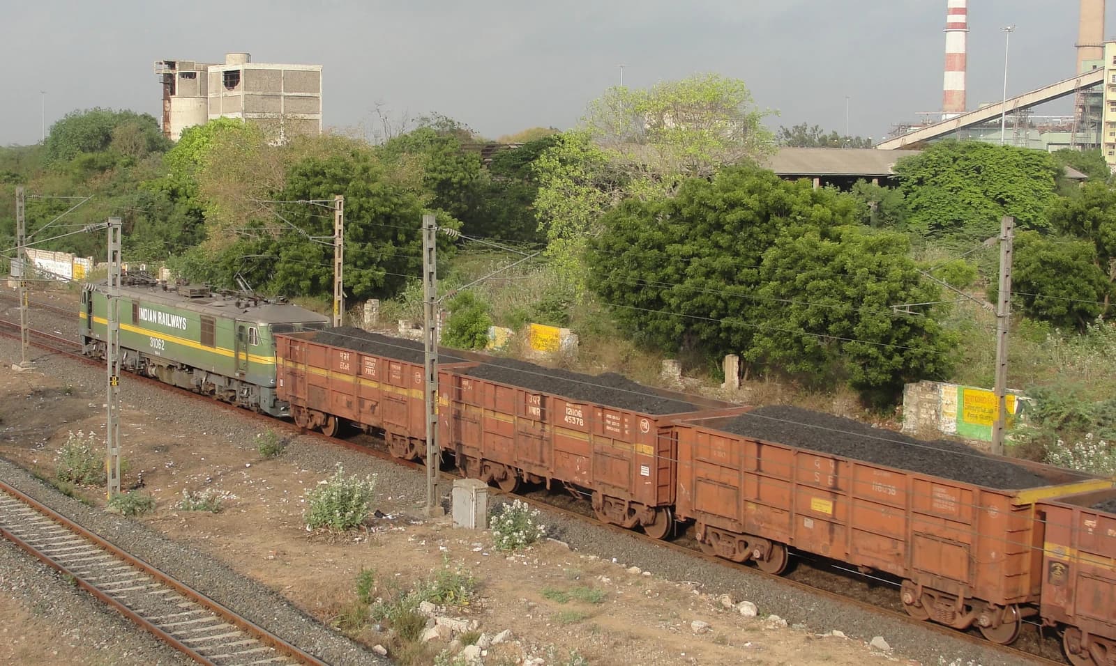 An Indian Railways locomotive pulls wagons filled with coal along train tracks.