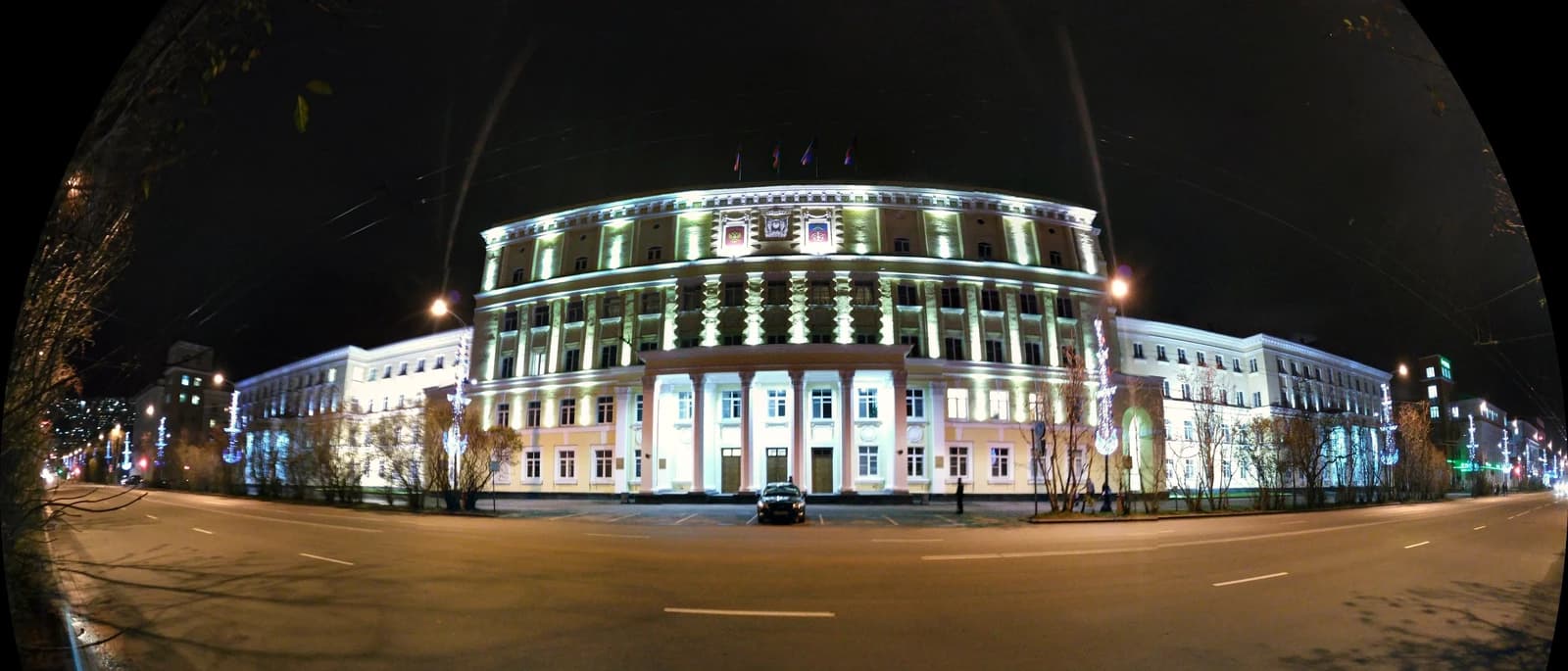 The Murmansk City Administration building illuminated at night, with a street in the foreground.