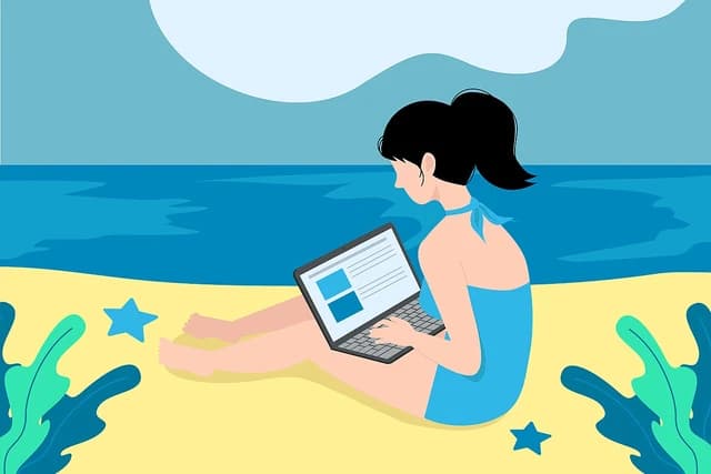 Woman working on a laptop while sitting on a sandy beach by the ocean.