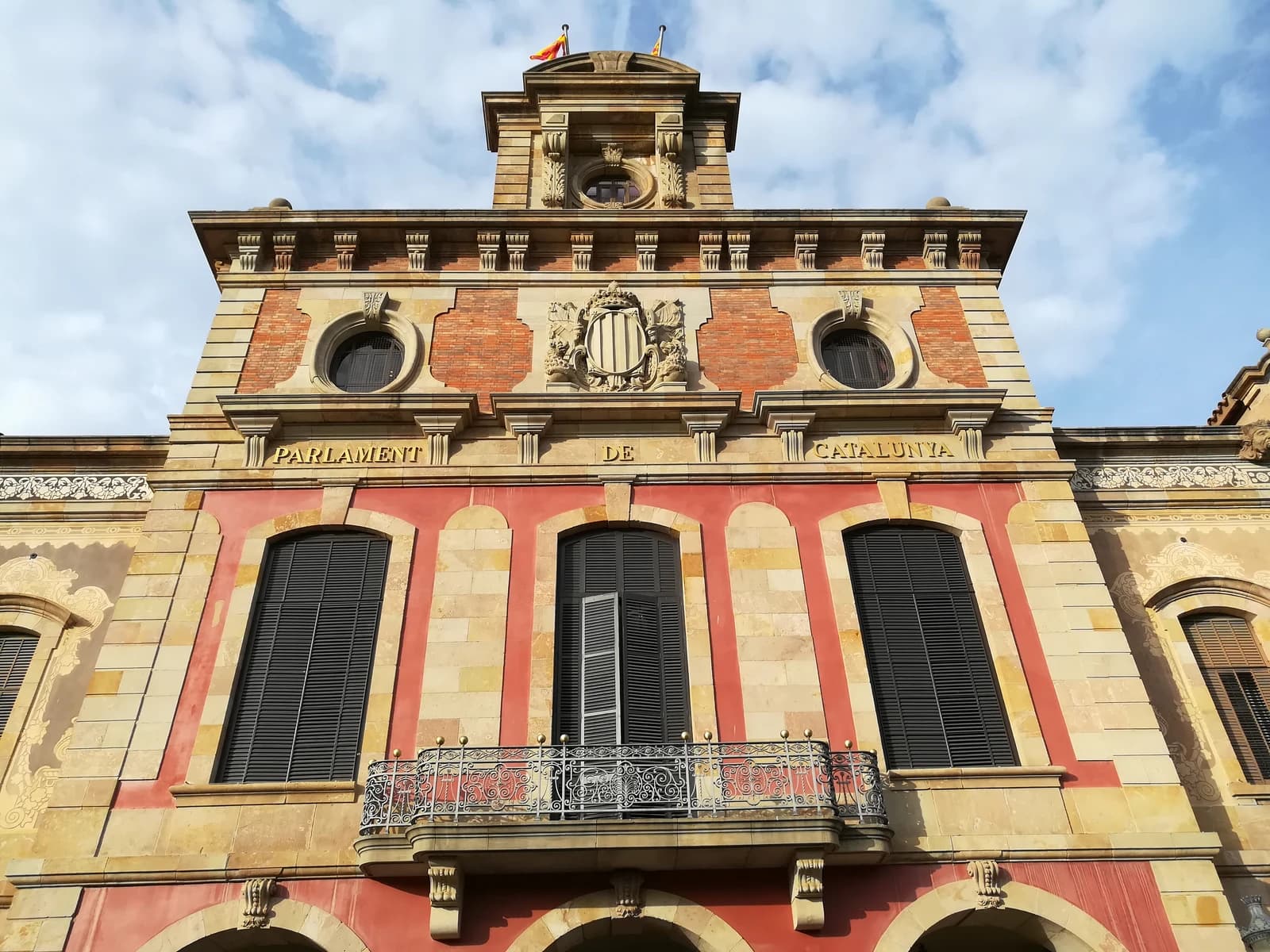 Exterior facade of the Palau del Parlament de Catalunya building under a partly cloudy sky.