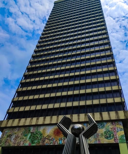 Bangladesh Bank main building, a tall structure with many windows, seen from below.