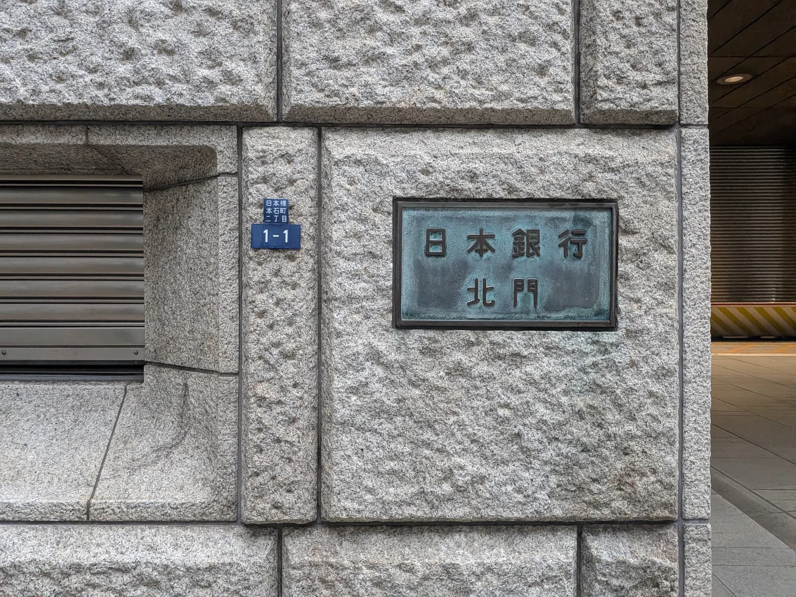Close-up of a bronze plaque on a stone wall displaying the Bank of Japan's name in Japanese characters.