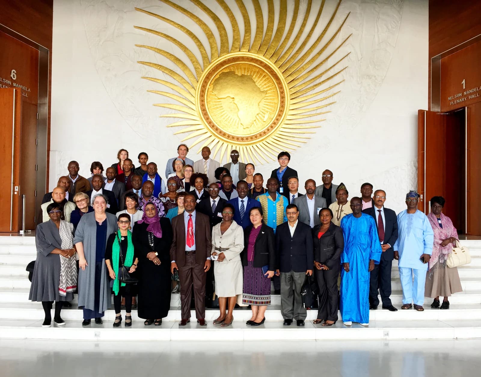 A group of delegates stands on steps in front of the African Union emblem.