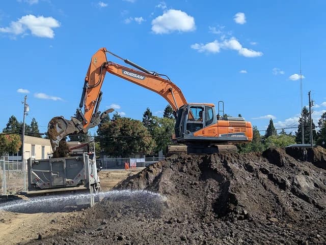 Doosan DX 225 LC excavator loading dirt into a dump truck at a job site.