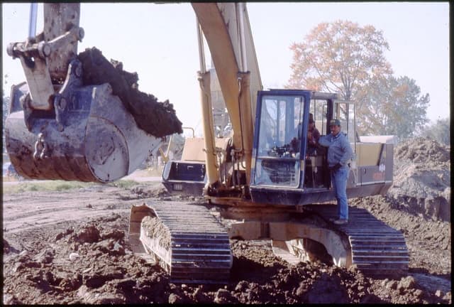 Construction workers operating an excavator at a worksite.