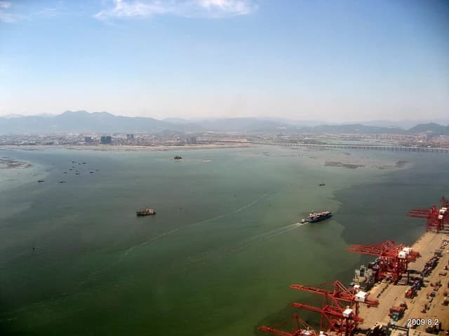 Aerial view of Xiamen container terminal, showing red cranes and ships loading or unloading cargo.
