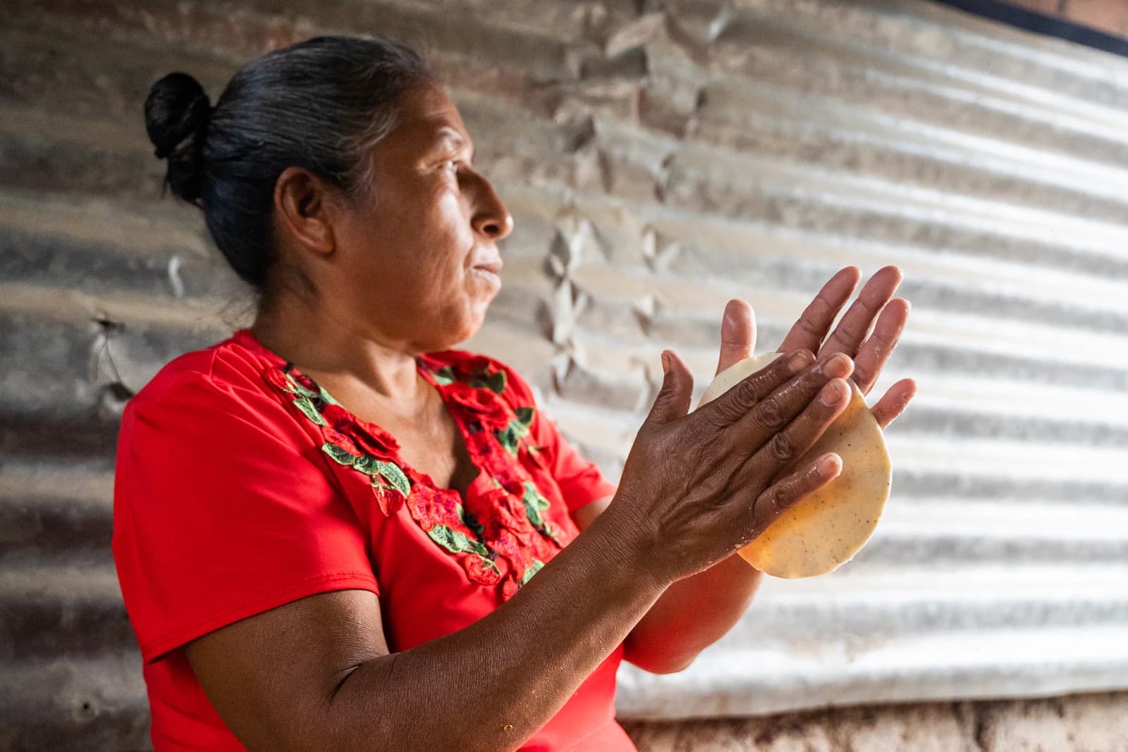 Woman in red shirt shaping tortilla dough with her hands.