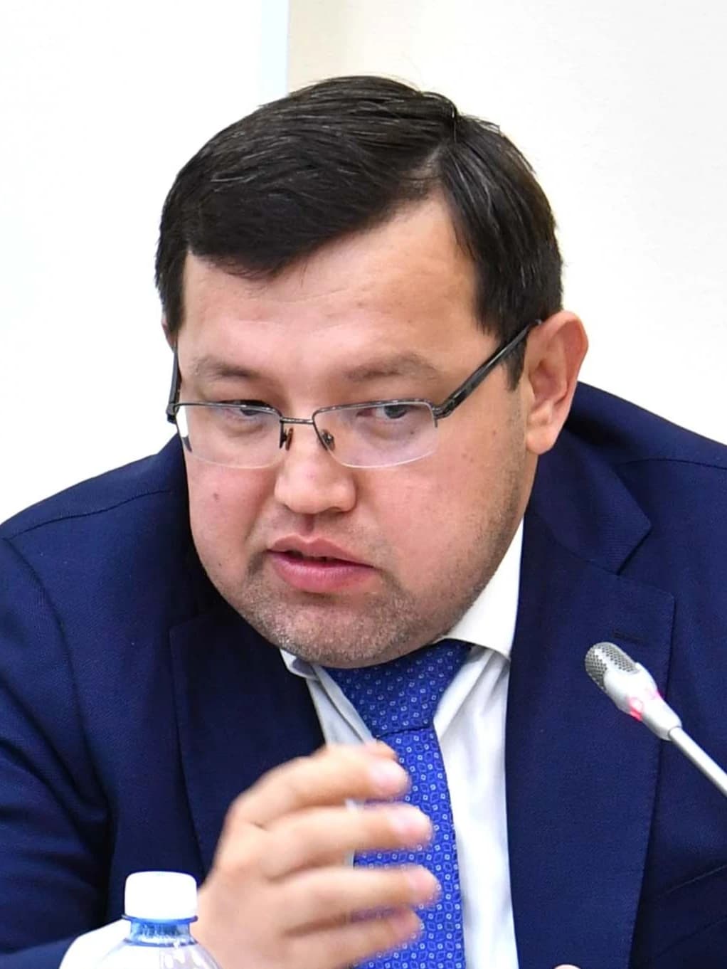 Oljas Qudaybergenov, economist, speaking into a microphone at an event.