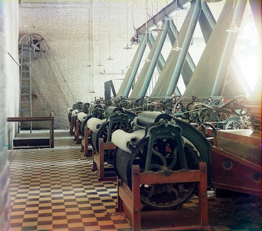 Textile machines producing cotton thread in a mill interior.