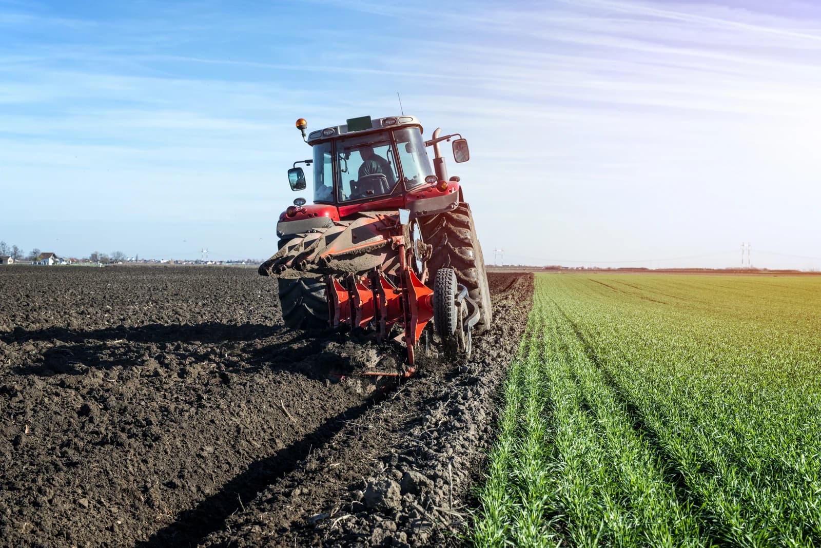Red tractor with attached plow cultivating dark brown soil in an open field.