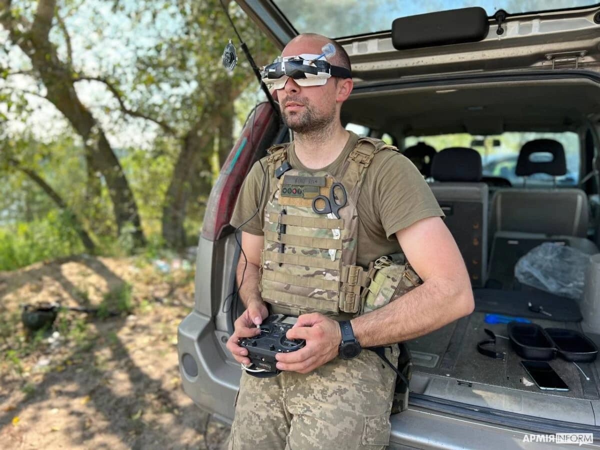 Ukrainian soldier wearing FPV goggles and holding a drone remote control outdoors.