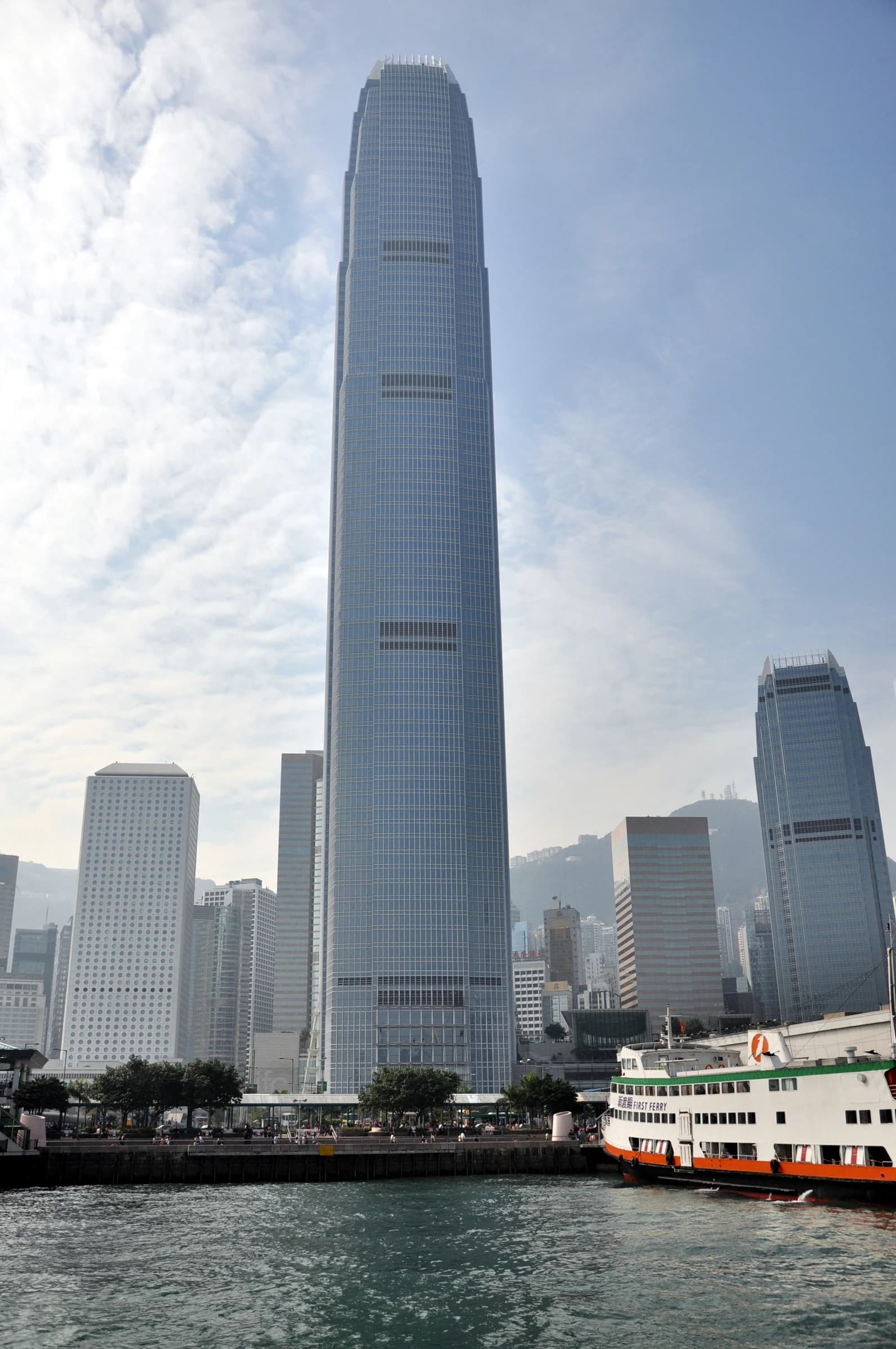 The Two International Finance Centre skyscraper towering over Hong Kong harbor, with a ferry in the foreground.