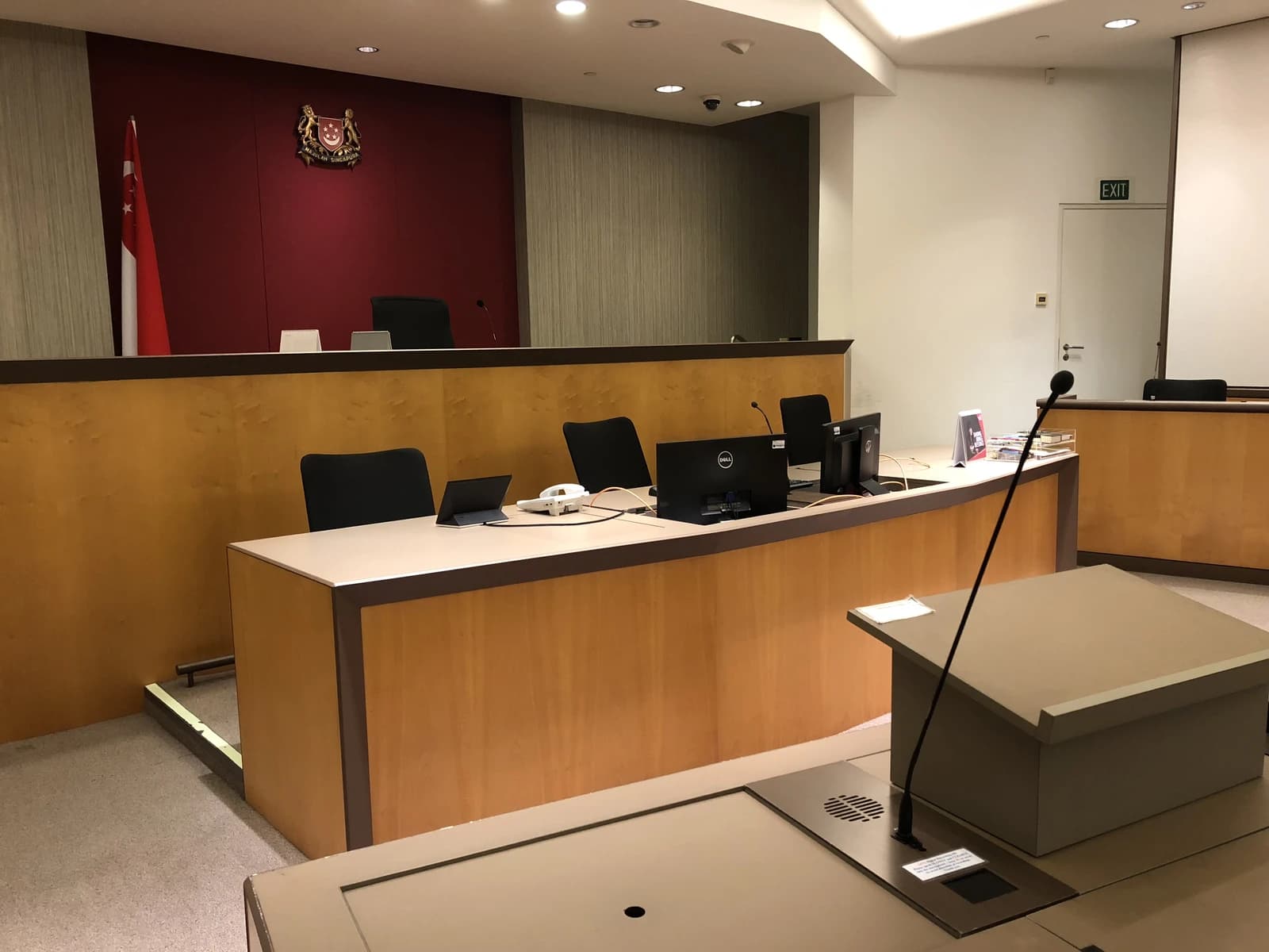 An empty courtroom in the Supreme Court of Singapore with benches and a flag.